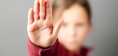Kind in einer roten Jacke streckt die Hand aus, zeigt fünf Finger und sagt Stopp