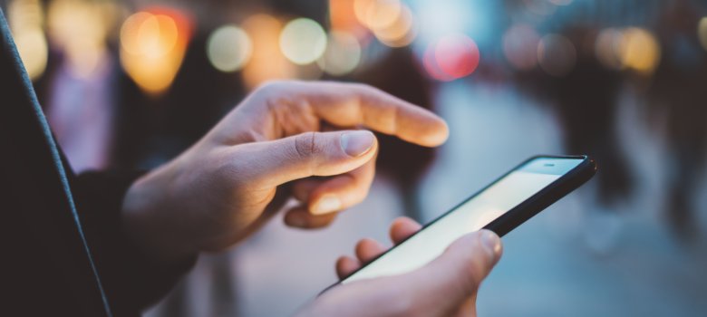 Closeup of male hands typing an sms message via smartphone outside, hipster man enjoying evening walk and using his cellphone, bokeh lights